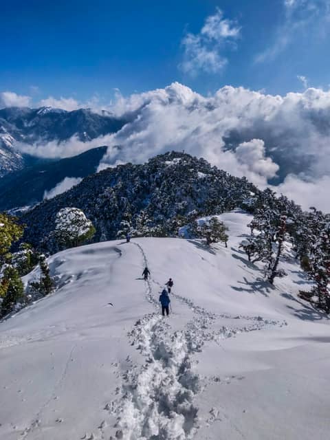 Trekkers walking a snow ridge above the clouds